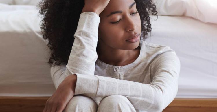 Young black woman sitting against bed with headache